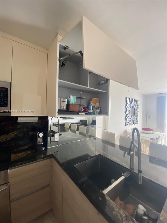 kitchen featuring stainless steel microwave, dark stone counters, and a sink