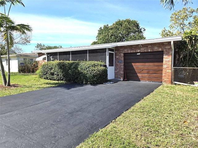 view of front of home with brick siding, an attached garage, a front yard, a sunroom, and driveway