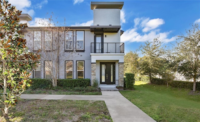 view of front facade featuring a balcony, stucco siding, and a front yard