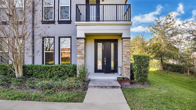 doorway to property with a balcony, a yard, stone siding, and stucco siding