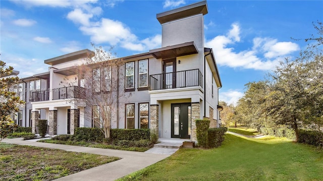 townhome / multi-family property with stone siding, a balcony, a front lawn, and stucco siding