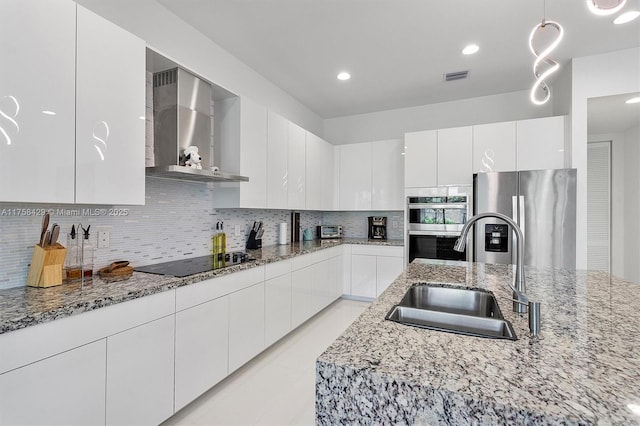 kitchen featuring stainless steel appliances, a sink, visible vents, white cabinets, and wall chimney range hood