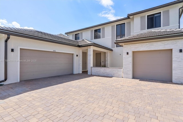 view of front of house with stucco siding, a garage, a tiled roof, and decorative driveway