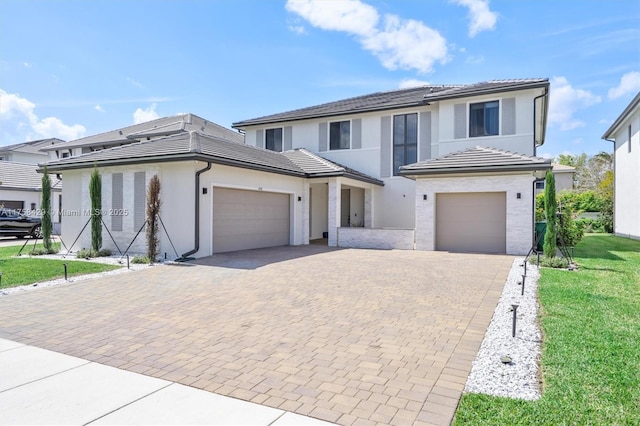 traditional-style house featuring stucco siding, a tiled roof, decorative driveway, a front yard, and a garage