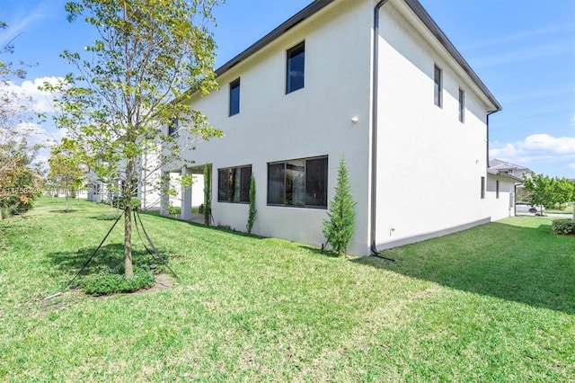 back of house with a lawn and stucco siding