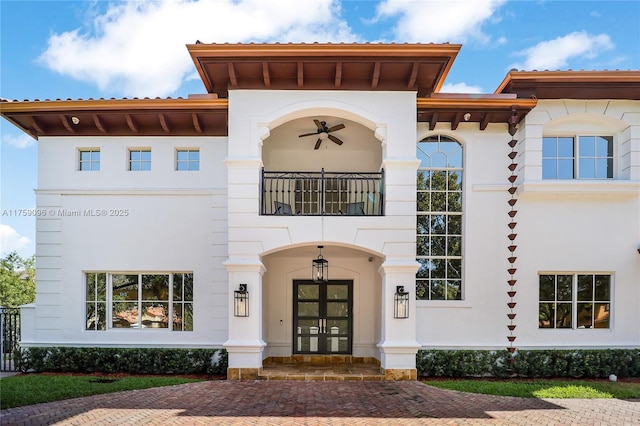 view of front facade with stucco siding, a balcony, and french doors