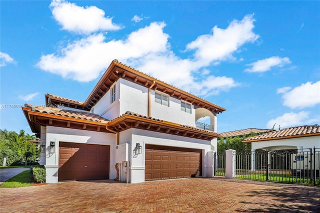 mediterranean / spanish-style home featuring an attached garage, fence, decorative driveway, a gate, and stucco siding