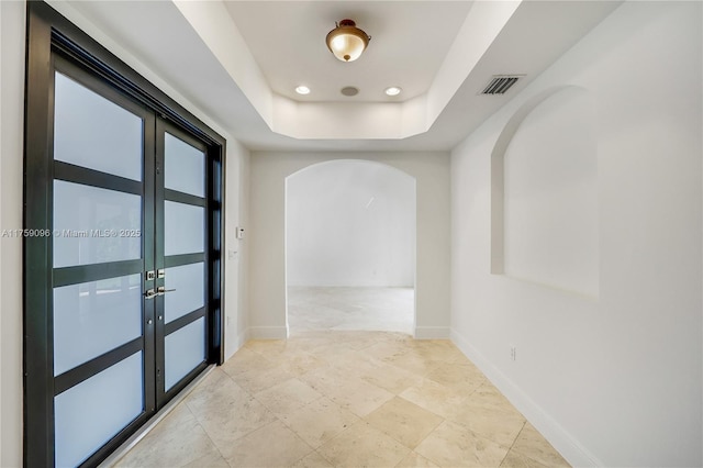 corridor with arched walkways, a raised ceiling, visible vents, and baseboards