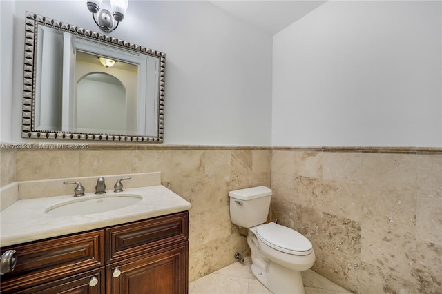 half bathroom featuring wainscoting, toilet, tile patterned flooring, vanity, and tile walls