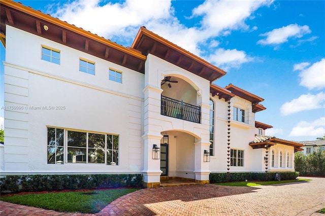 mediterranean / spanish home featuring a ceiling fan, a balcony, and stucco siding