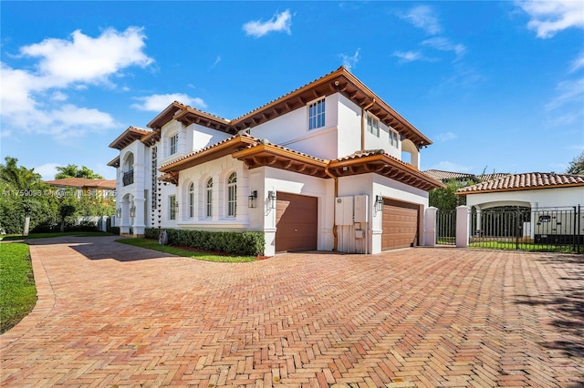 mediterranean / spanish-style home featuring a garage, a tiled roof, decorative driveway, a gate, and stucco siding