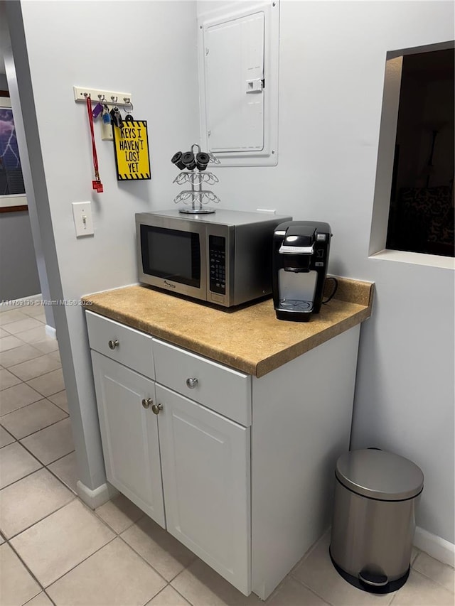 bar with electric panel, stainless steel microwave, baseboards, and light tile patterned floors