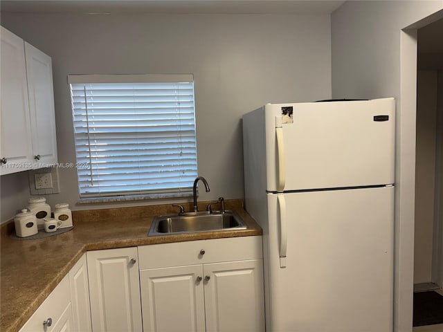 kitchen with dark countertops, white cabinets, freestanding refrigerator, and a sink