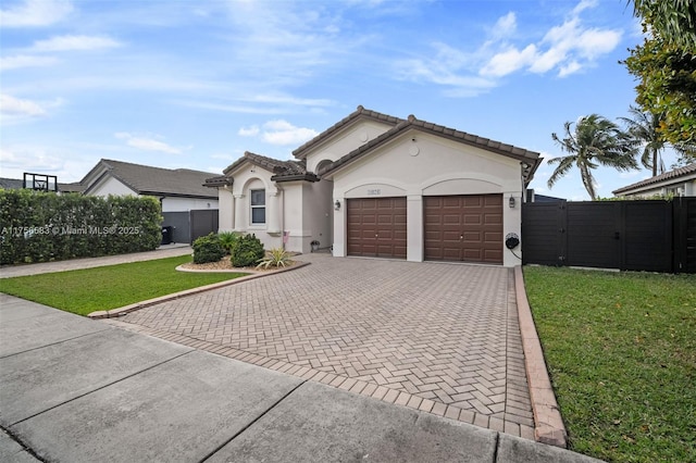 mediterranean / spanish house featuring an attached garage, decorative driveway, a gate, stucco siding, and a front yard