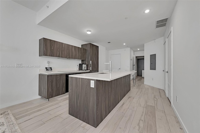 kitchen featuring light wood-style flooring, visible vents, dark brown cabinets, light countertops, and modern cabinets