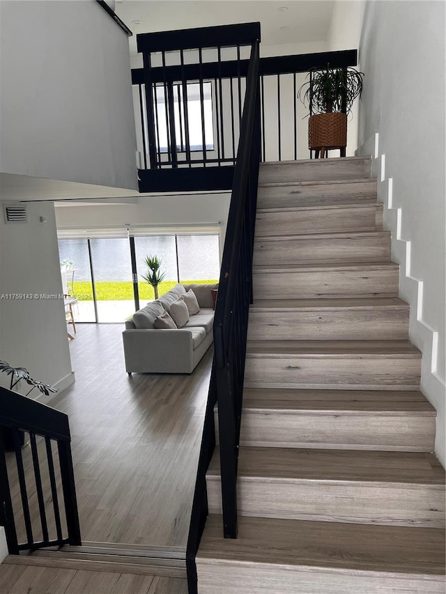 stairway with visible vents, a high ceiling, and wood finished floors