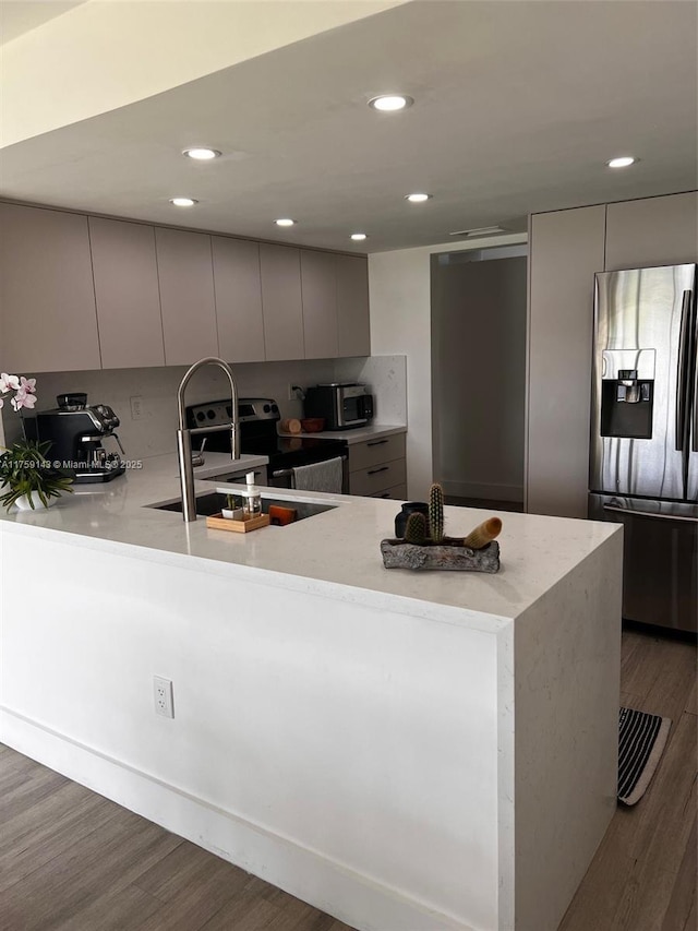 kitchen featuring a peninsula, a sink, wood finished floors, appliances with stainless steel finishes, and modern cabinets