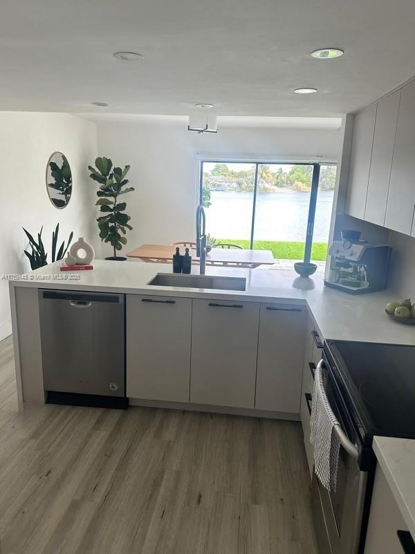 kitchen featuring appliances with stainless steel finishes, light countertops, light wood-style floors, white cabinetry, and a sink