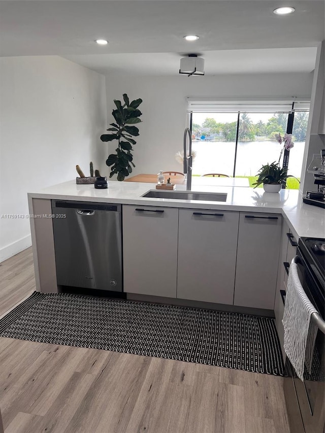 kitchen featuring range, light countertops, light wood-type flooring, stainless steel dishwasher, and a sink