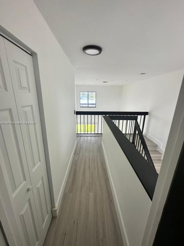 hall featuring light wood-style flooring, baseboards, and an upstairs landing