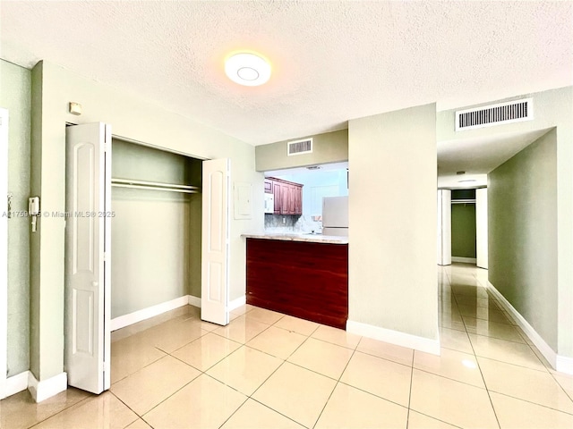 unfurnished bedroom featuring light tile patterned floors, visible vents, freestanding refrigerator, and a closet