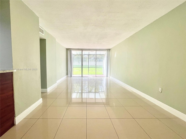 empty room with visible vents, baseboards, expansive windows, light tile patterned floors, and a textured ceiling