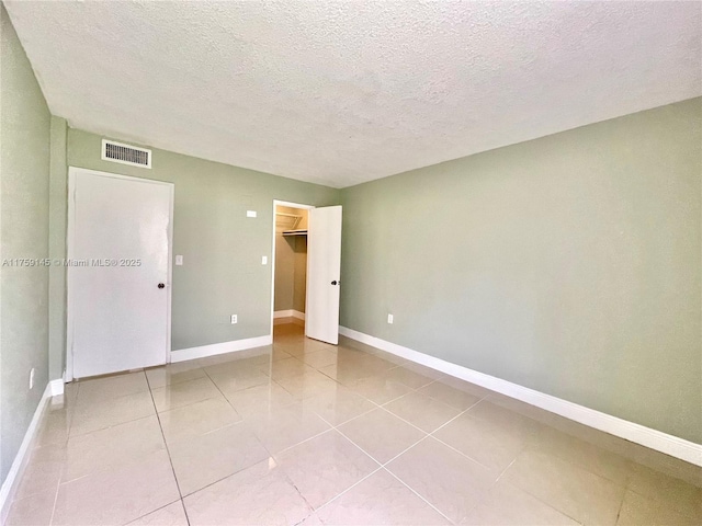 unfurnished bedroom with tile patterned flooring, baseboards, visible vents, and a textured ceiling