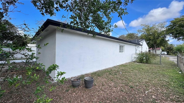 view of home's exterior with stucco siding, a lawn, and fence