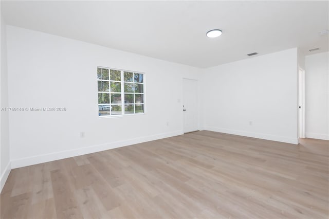 empty room with light wood finished floors, visible vents, and baseboards