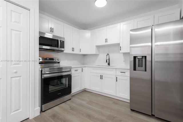 kitchen featuring white cabinets, stainless steel appliances, light countertops, light wood-type flooring, and a sink