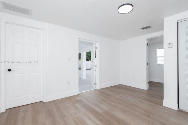 spare room with light wood finished floors, visible vents, and baseboards