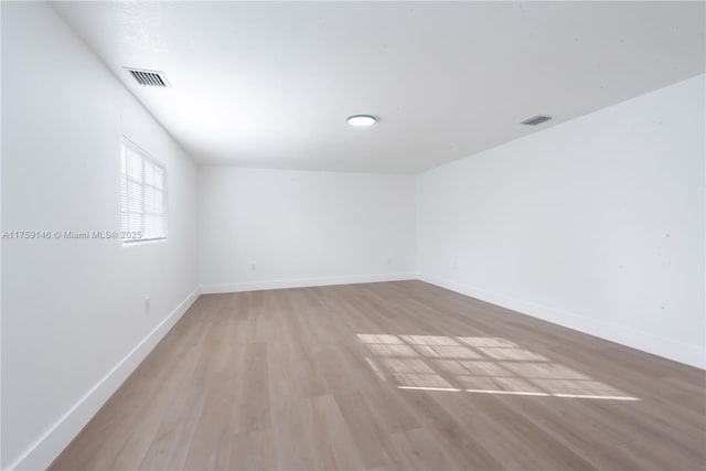 spare room with light wood-type flooring, visible vents, and baseboards