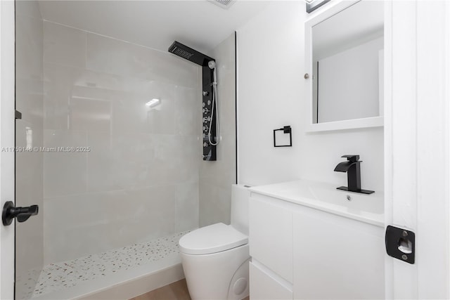 bathroom featuring toilet, a tile shower, and vanity