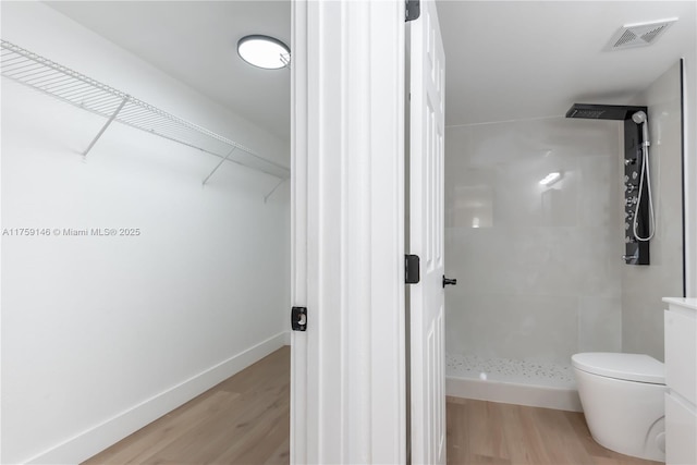 bathroom featuring visible vents, toilet, wood finished floors, a shower stall, and a spacious closet