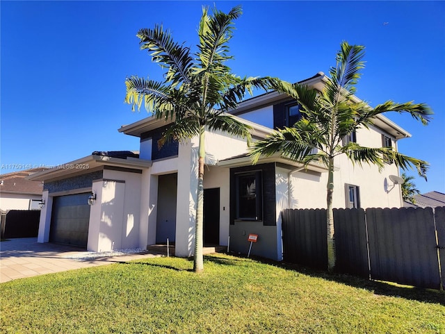 view of front facade featuring fence, a front yard, stucco siding, decorative driveway, and an attached garage