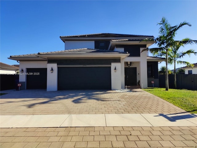 prairie-style house with decorative driveway, fence, a garage, and stucco siding