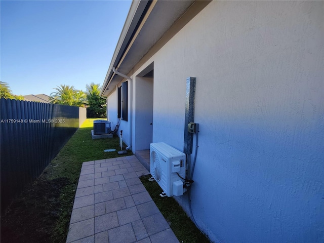 view of side of home with fence, ac unit, central AC unit, stucco siding, and a yard