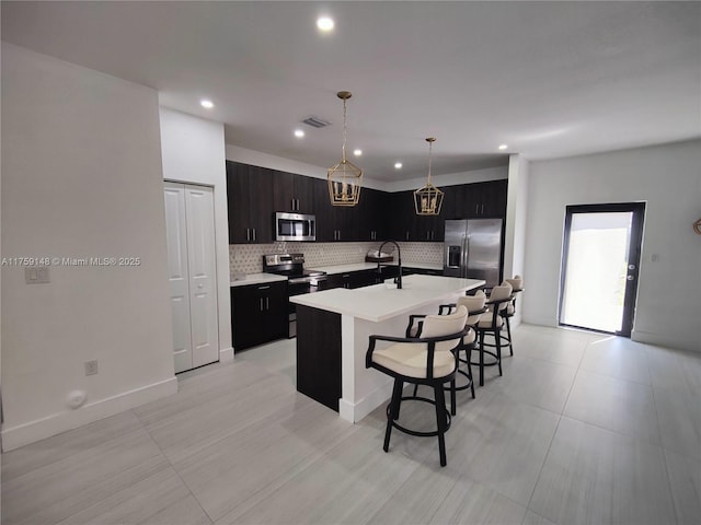 kitchen with backsplash, a center island with sink, light countertops, a kitchen breakfast bar, and stainless steel appliances