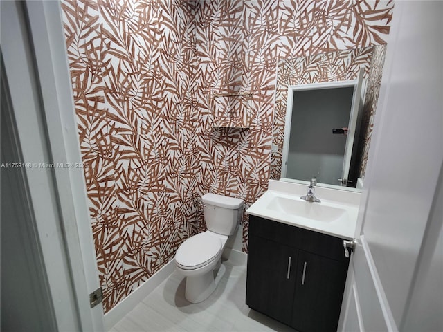 bathroom with wallpapered walls, toilet, vanity, and baseboards