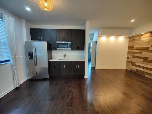 kitchen with baseboards, dark wood-style flooring, a sink, stainless steel appliances, and light countertops