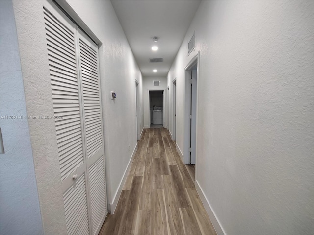 corridor featuring visible vents, wood finished floors, baseboards, and a textured wall