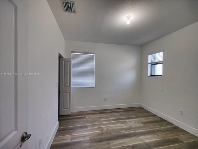 unfurnished room with visible vents, baseboards, and dark wood-style flooring