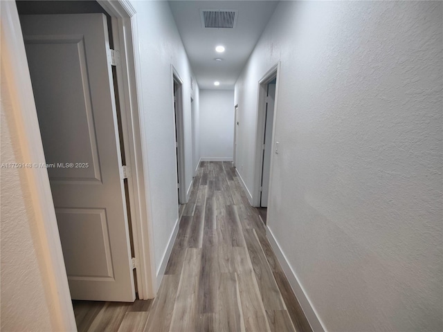 hall with visible vents, baseboards, and wood finished floors