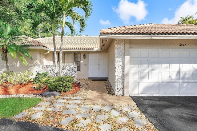 view of front facade featuring an attached garage, a tiled roof, aphalt driveway, and stucco siding