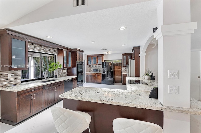 kitchen with black appliances, tasteful backsplash, a peninsula, and dark brown cabinets