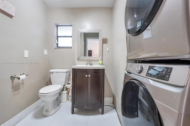 bathroom with toilet, vanity, baseboards, tile patterned floors, and stacked washer and clothes dryer