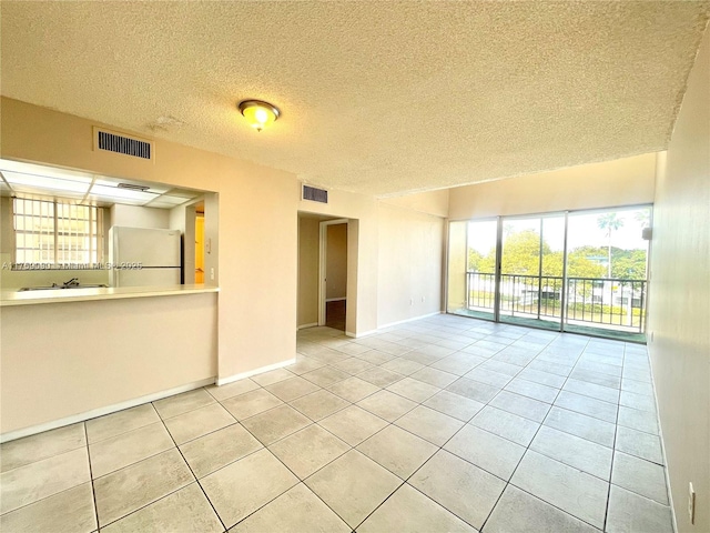 tiled spare room with visible vents, a textured ceiling, and baseboards