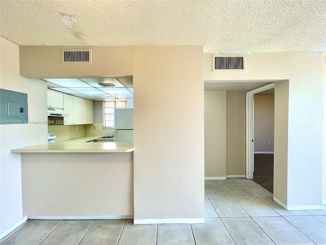 kitchen featuring under cabinet range hood, visible vents, light countertops, and freestanding refrigerator