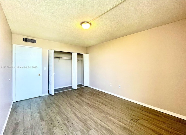 unfurnished bedroom featuring a closet, visible vents, baseboards, and wood finished floors