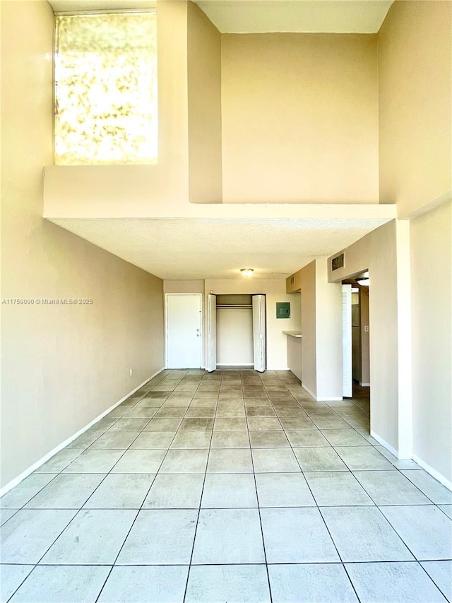 spare room with light tile patterned flooring, baseboards, visible vents, and a towering ceiling